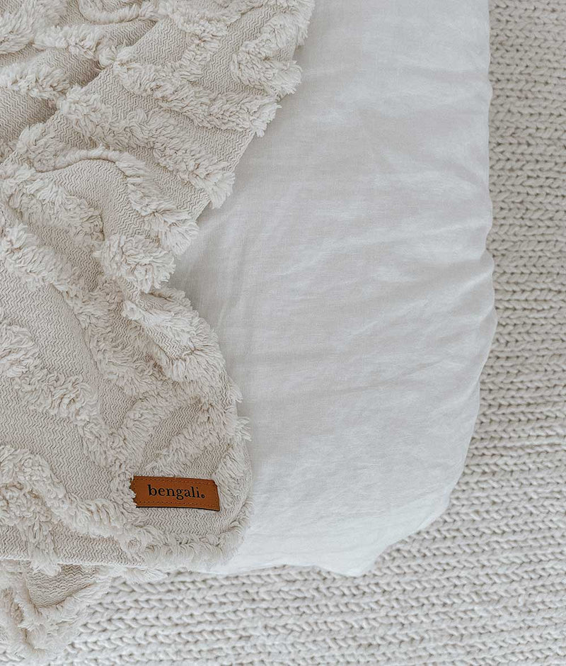 A white IVORY TUFTED THROW blanket on a bed with an Oeko-tex® Certified label, Bengali Collections.