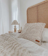 An IVORY TUFTED THROW with a wicker headboard and pillows, made from pure cotton, by Bengali Collections.