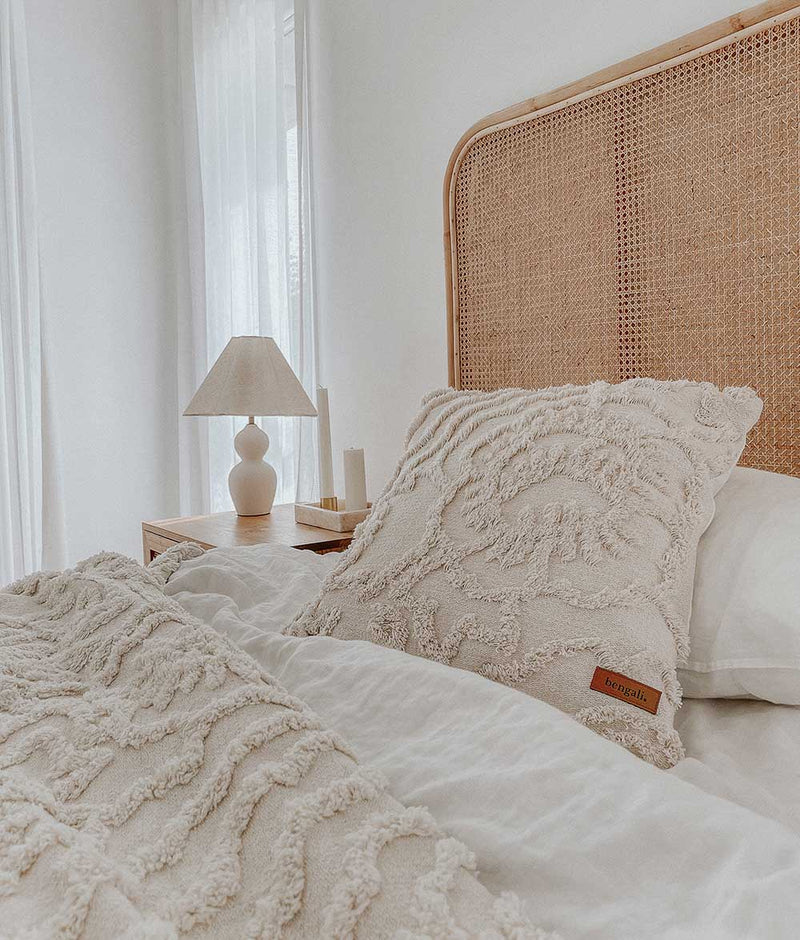 An IVORY TUFTED THROW with a wicker headboard and pillows, made from pure cotton, by Bengali Collections.