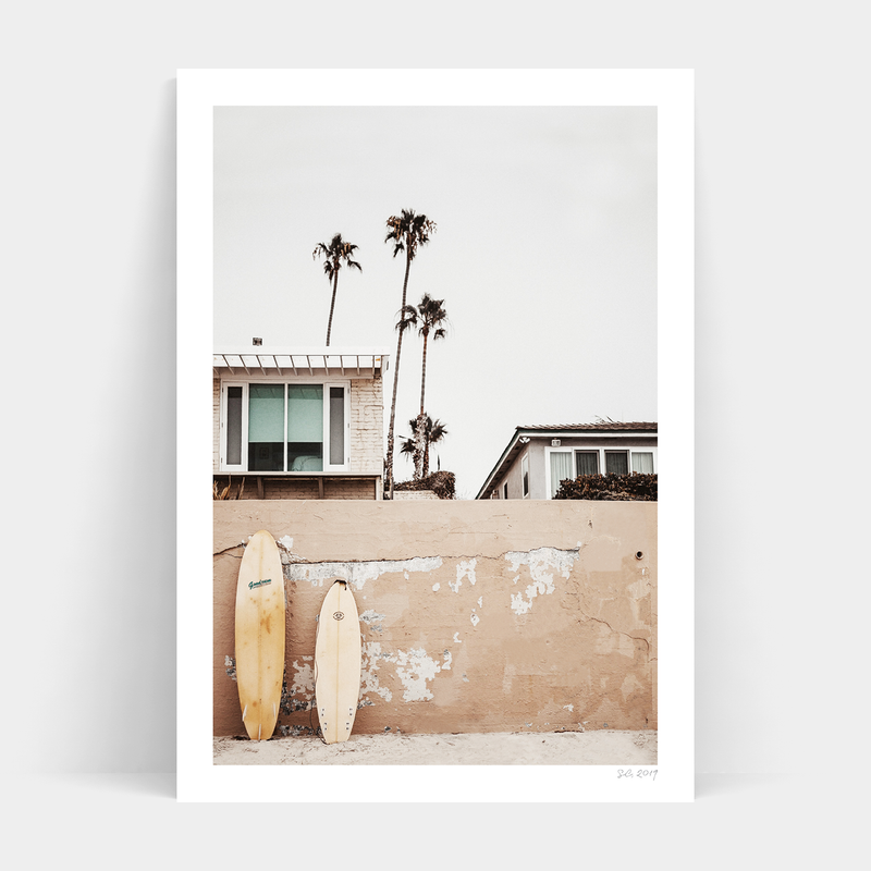 Two Beachfront surfboards leaning against a wall, available for delivery.
