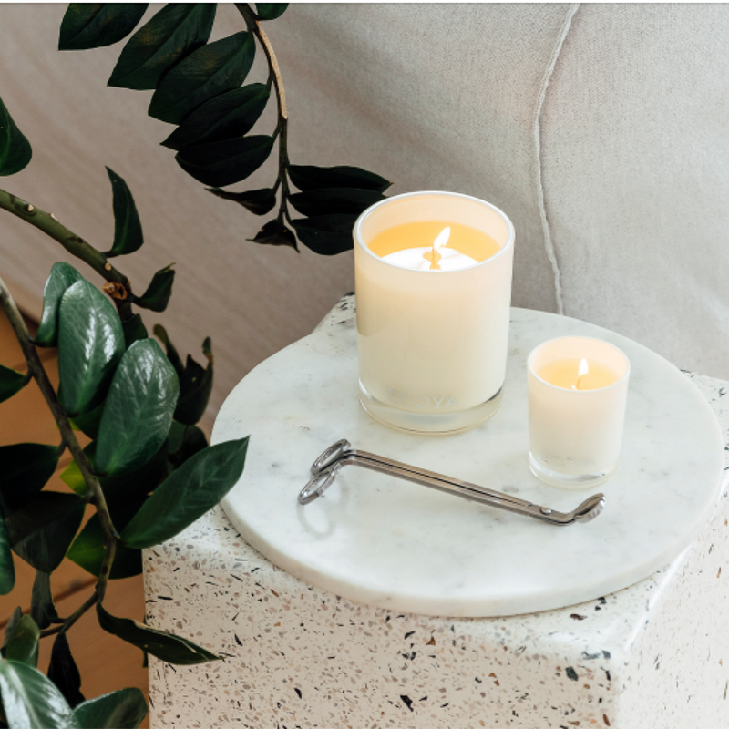 An Ecoya Wick Trimmer, designed for home fragrance, sits on top of a marble table next to a plant.