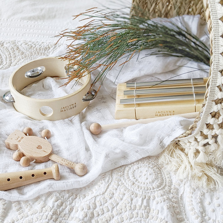 Wooden musical toys and a tambourine on a white bed with a basket and dried grasses