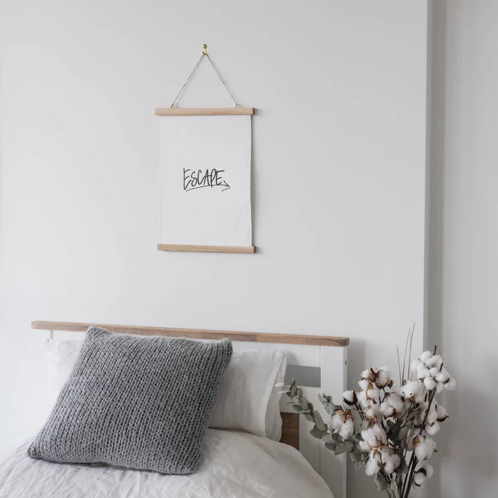A wanderlust-inspired bedroom with an eco-friendly wall hanging, the Escape Print by AXEL & ASH, and a cozy bed with pillows.