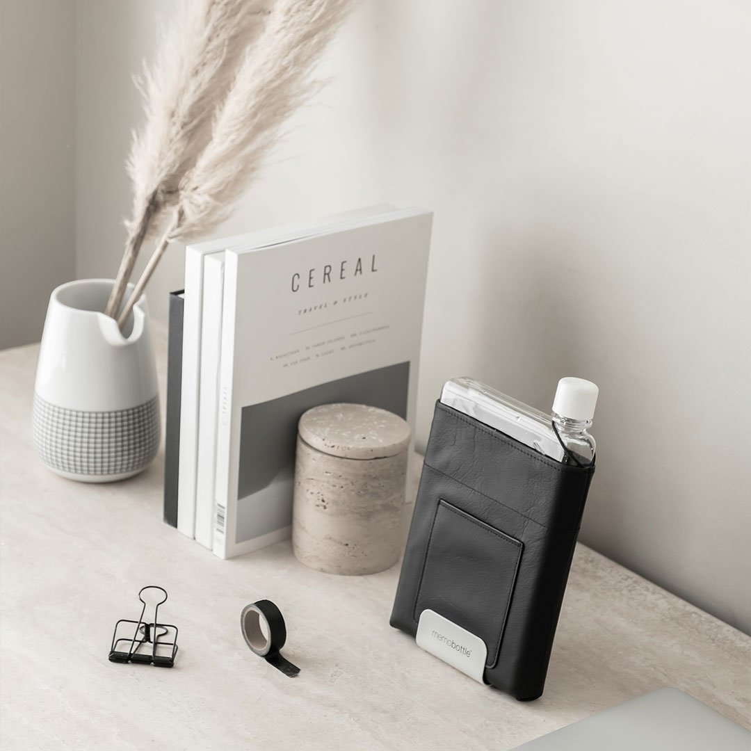 Memobottle in a black sleeve in a white desk stand, styled with books and a concrete pot