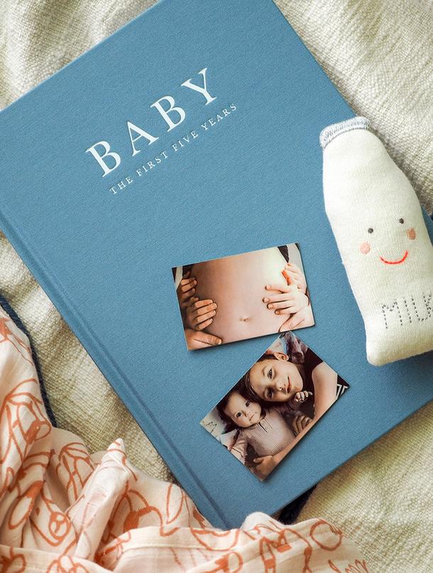 Blue Write To Me Baby journal with baby photos and a milk bottle on a soft blanket