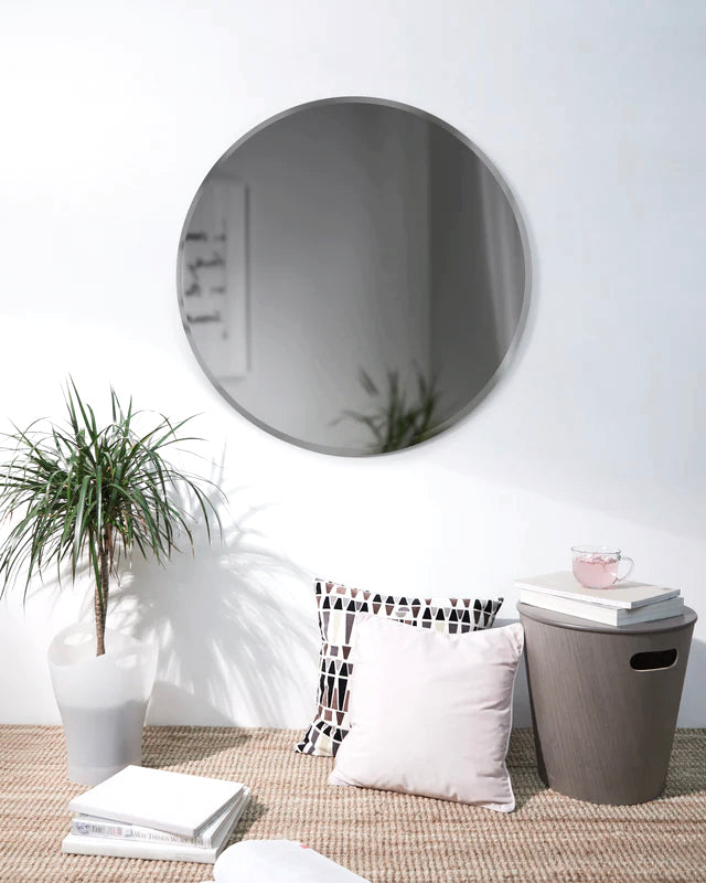 Umbra Bevy round mirror in smoke glass on a white wall above cushions and a plant