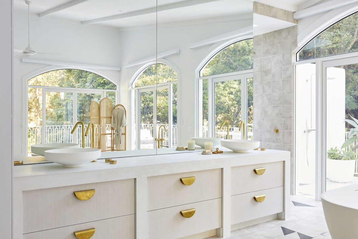 White bathroom vanity with gold handles below arched windows