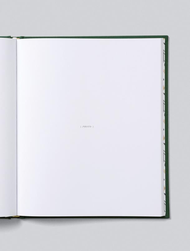 Christmas Family Book open to its first blank page, with the forest green linen cover