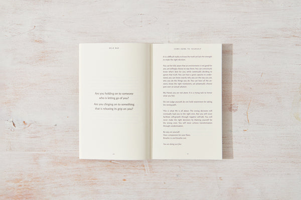 An open book on a wooden surface, showcasing Come Home to Yourself | Déjà Rae books in a serene setting that evokes feelings of solitude by Thought Catalog.