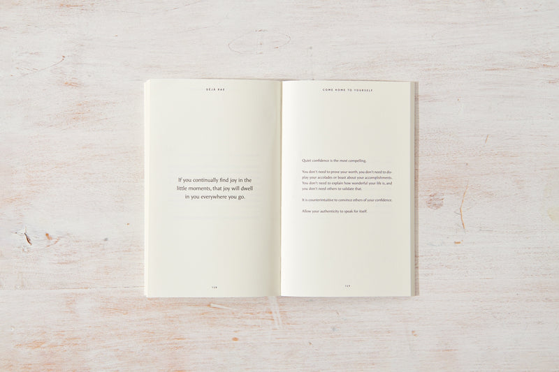 A "Come Home to Yourself | Déjà Rae" design and lifestyle book placed on a wooden surface, by Thought Catalog.