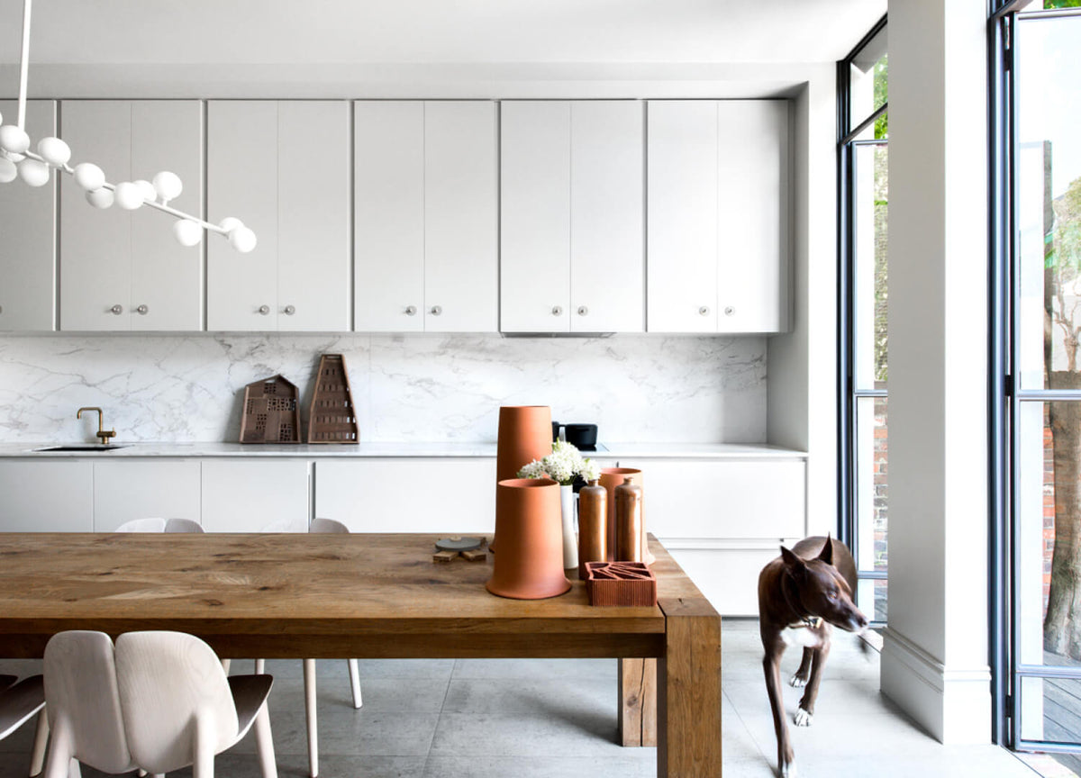 Dog beside a long timber dining table in a white kitchen
