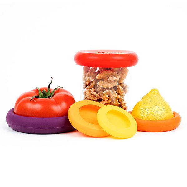 Silicone Food Huggers covering a cut tomato and lemon, with one used as a lid on a jar of walnuts