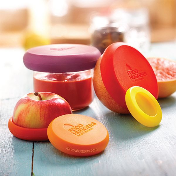 Food Huggers covering a jar, a cut apple and a grapefruit on a pale blue timber table