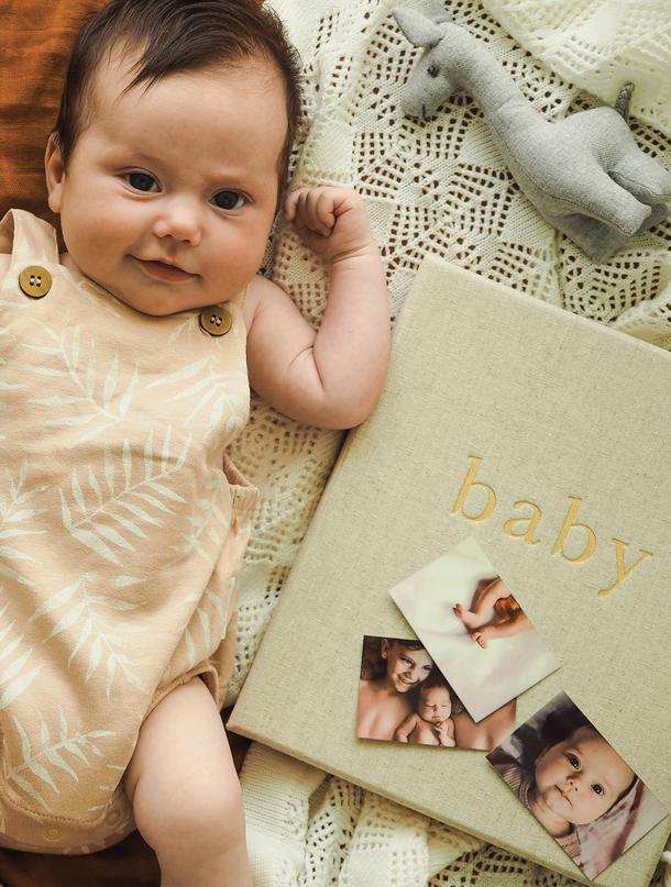 Baby lying on a knitted blanket beside the oatmeal Write To Me baby journal and photos