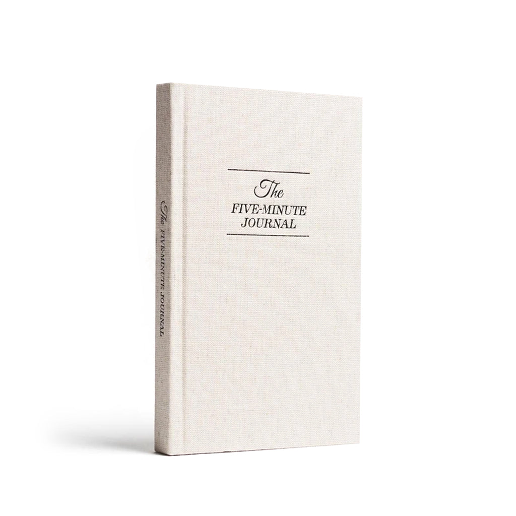 The Five Minute Journal in natural linen with a navy title, standing on white