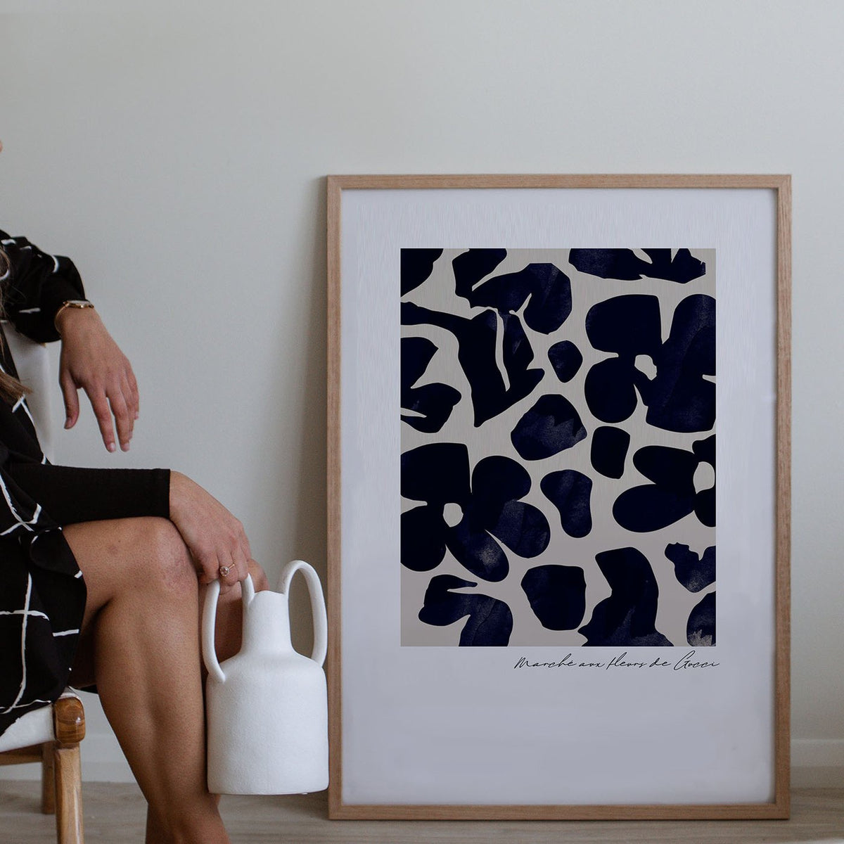 Navy flower market print in an oak frame on the floor beside a seated woman and a white jug