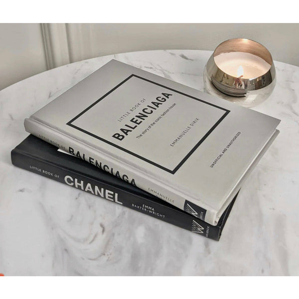 Two Little Books of Balenciaga on a table with a candle next to them.