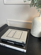 Little Book of Balenciaga books on a table next to a plant.