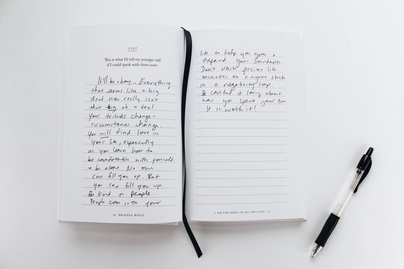 A "I Am The Hero Of My Own Life | Brianna Wiest" notebook with handwriting and a pen next to it, perfect for those who envision their ideal life and want to explore their unconscious attachments. Designed by Thought Catalog.