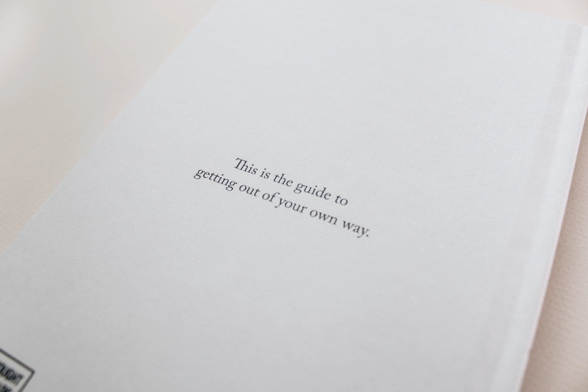 A white book with a quote on it, perfect for design and lifestyle enthusiasts or those looking to envision their ideal life. "I Am The Hero Of My Own Life" by Brianna Wiest, published by Thought Catalog explores the concept of unconscious attachments.