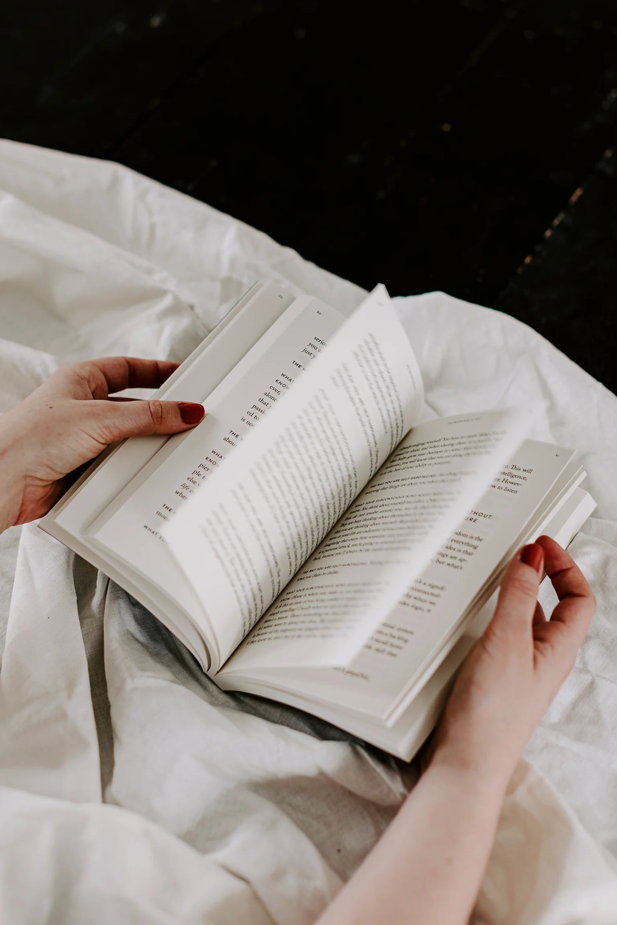 A woman is reading "The Mountain Is You" by Brianna Wiest on a bed.