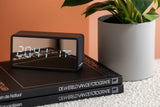 A Karlsson clock brand with an innovative design featuring graphics of an Alarm Mirror LED - Various Options sitting on top of a stack of books.