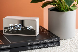 An Alarm Mirror LED - Various Options clock sitting on top of books.