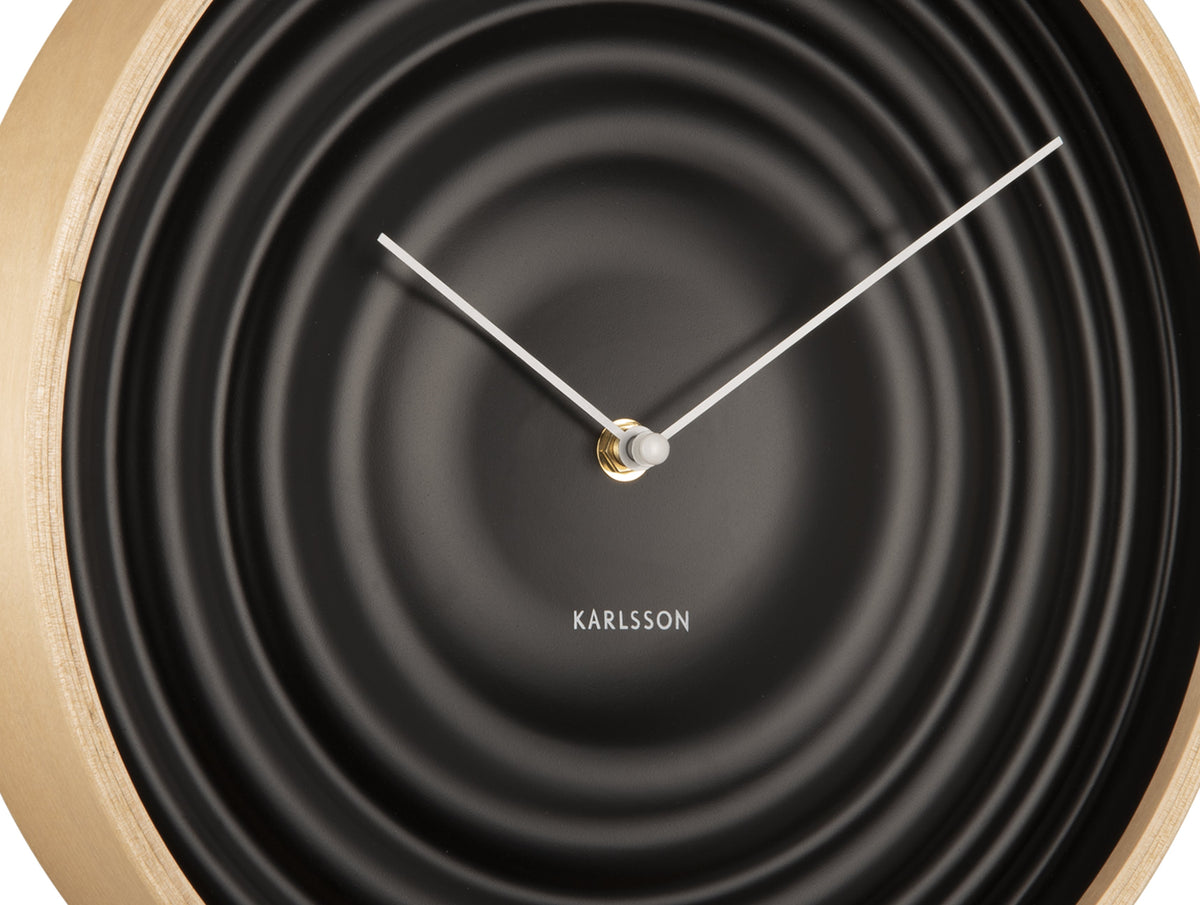 Close view of the black clock face showing the rippled rings and silver hands