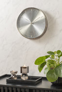 Silver Jewel wall clock on a textured white wall above a black fluted sideboard with a plant