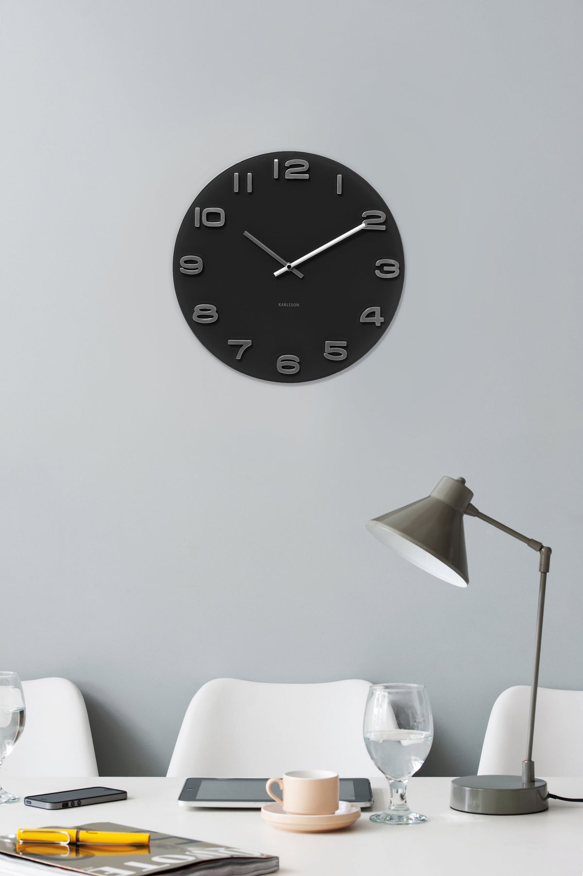 Black Karlsson Vintage clock on a pale grey wall above a white desk with a grey task lamp