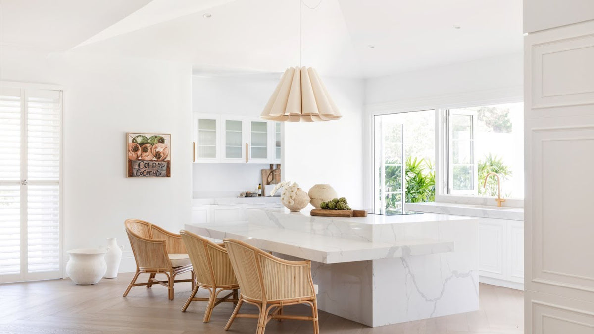 White kitchen island with rattan stools and a woven pendant