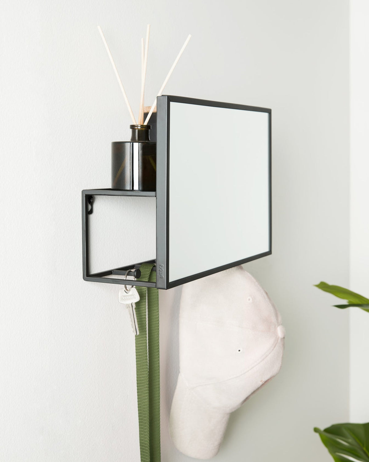 Black Umbra Cubiko mirror and organiser styled in an entryway with a hat and a plant.