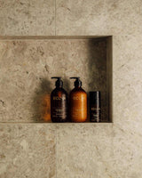 Two bottles of Ecoya Limited Edition Sandalwood & Amber Hand & Body Wash, providing home fragrance, sit on a shelf in a bathroom.
