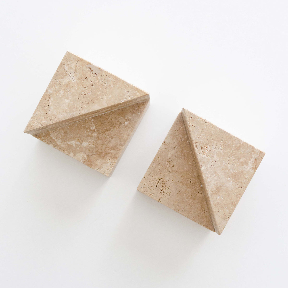 A pair of geometric travertine bookends on a white background, showing the angled wedge form