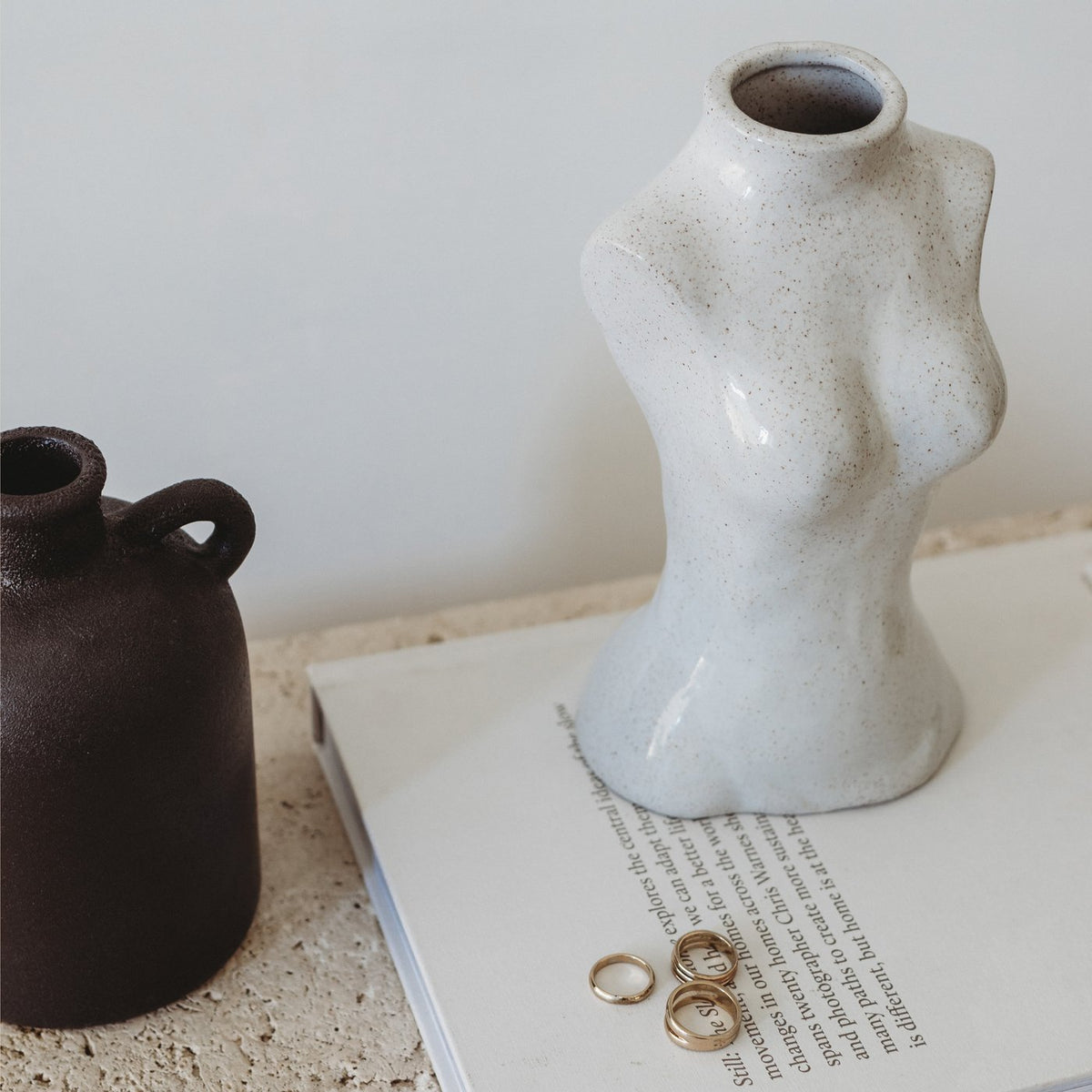 Female Silhouette Vase on books beside a dark jug and gold rings