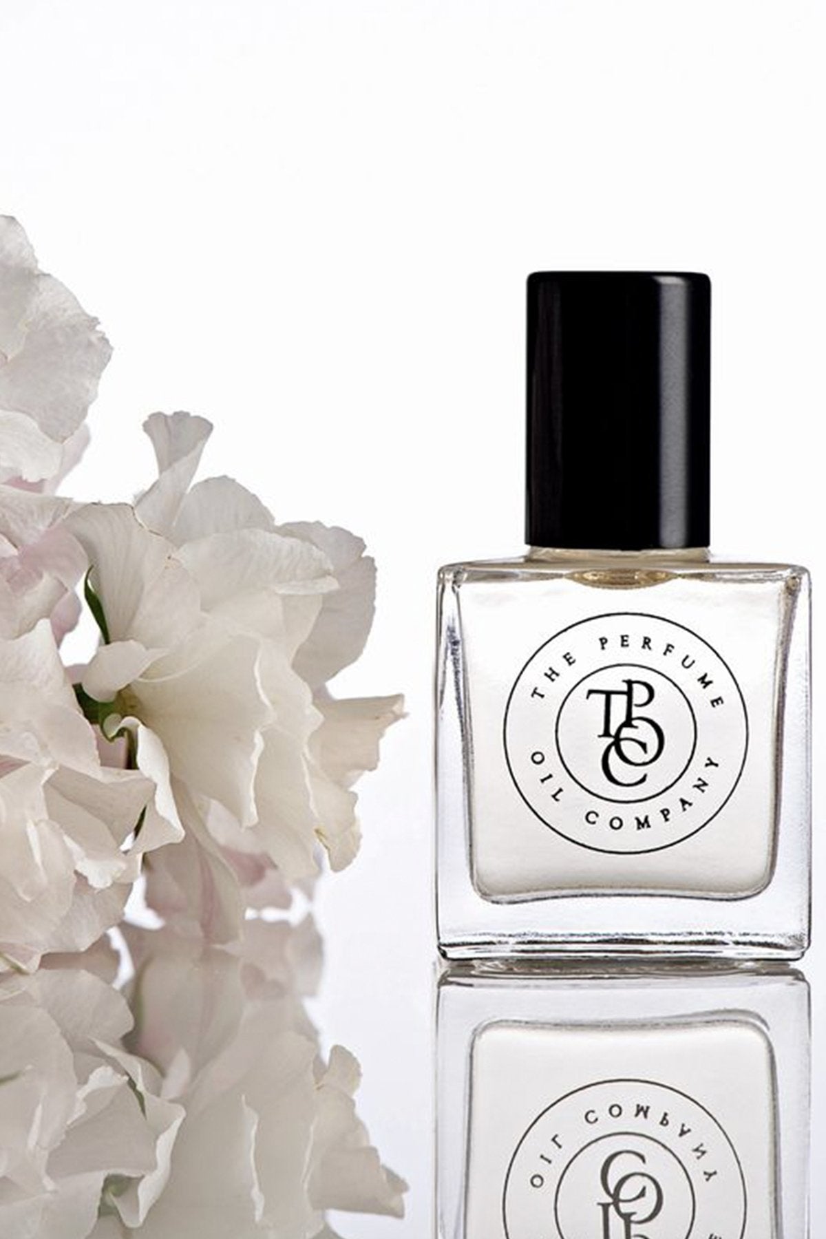 Perfume oil bottle beside soft white roses on a reflective surface