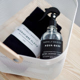 A basket with a bottle of Barkly Basics Sanitising Surface Spray and a black towel.