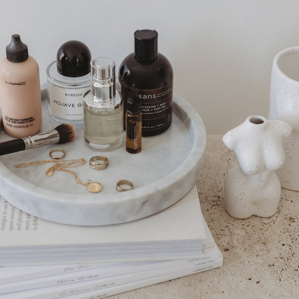 A Papier HQ Marble round tray with cosmetics and a book on it.