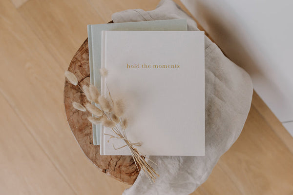 An Olive + Page - Hold The Moments Journal with the words hold the memories on top of a wooden table.