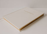 An Olive + Page - Hold The Moments Journal with gold lettering on a white surface.