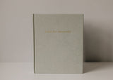 An Olive + Page - Hold The Moments Journal with gold lettering sits on a table.