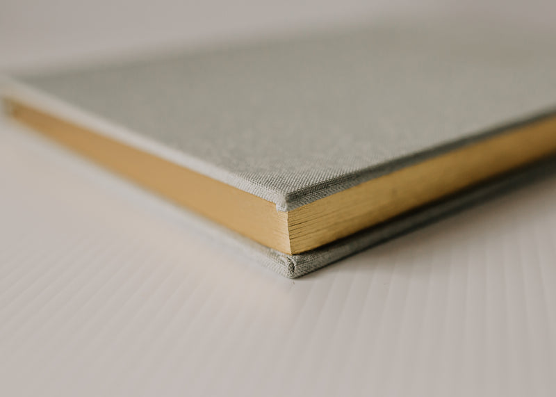 An Olive + Page - Hold The Moments Journal with a gold cover on a white surface.