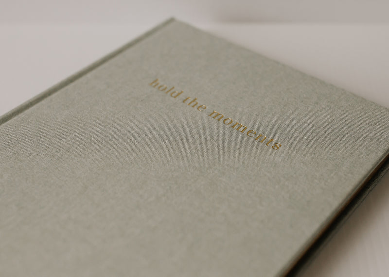 An Olive + Page - Hold The Moments Journal with the brand name Olive + Page on it.