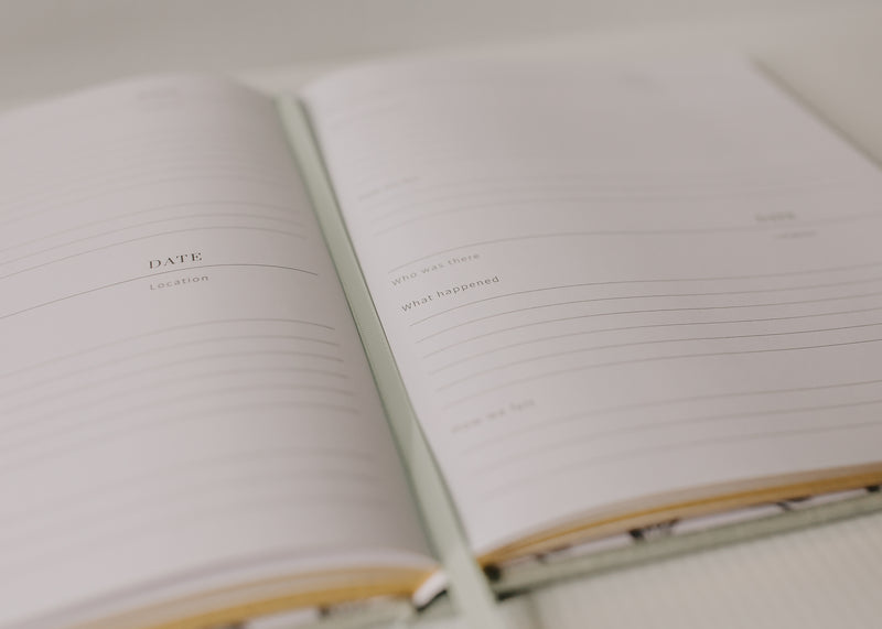A Olive + Page - Hold The Moments Journal is open on a white table, capturing a peaceful family moment.