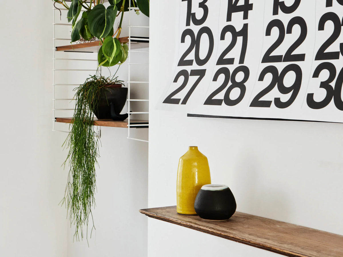 Stendig wall calendar styled above a timber console with plants and ceramics