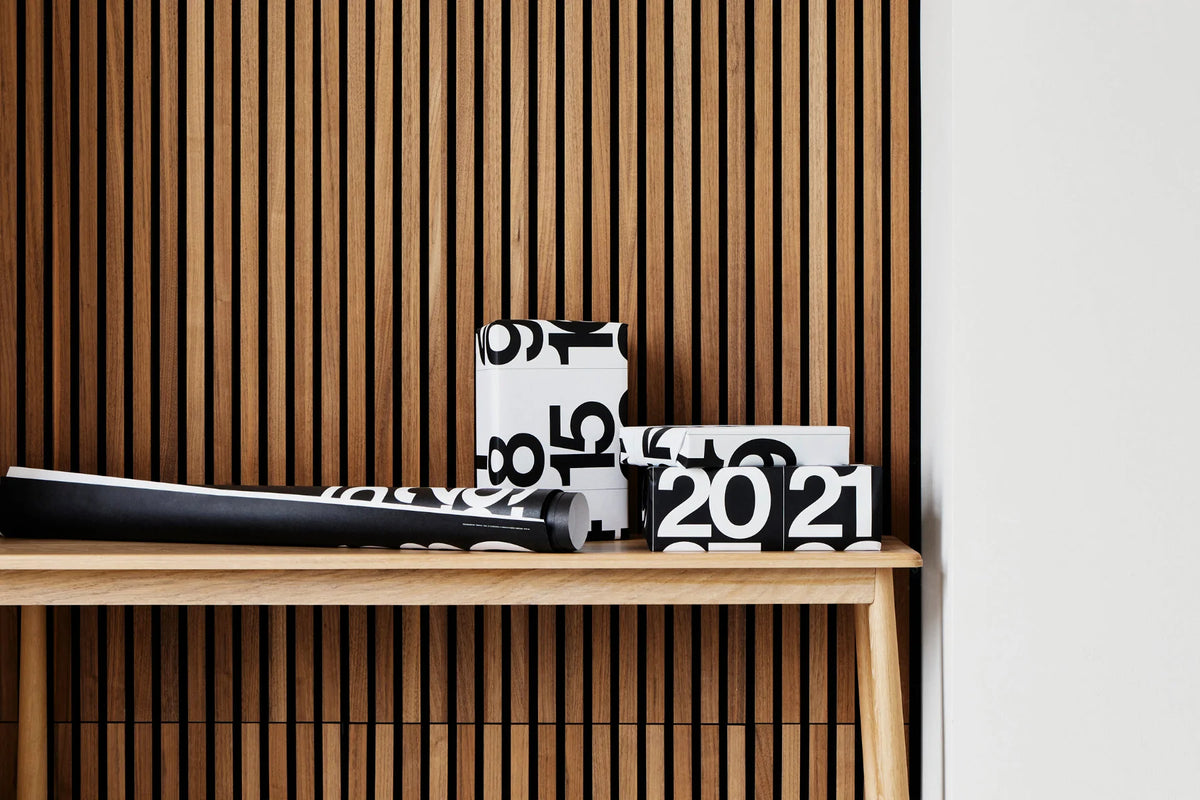 Torn Stendig Calendar pages styled as black and white gift wrap on boxes atop a timber console against a slat wall