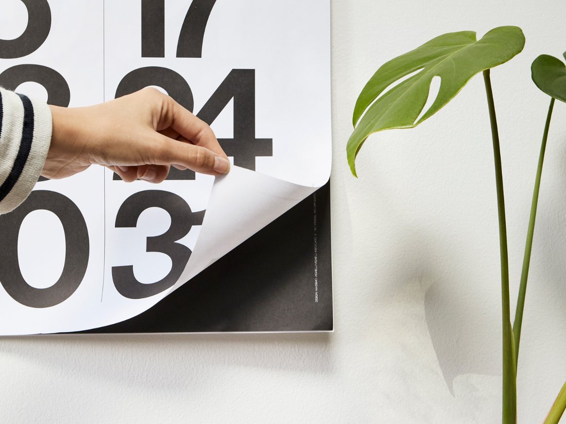 Hand holding the Stendig wall calendar beside a monstera plant