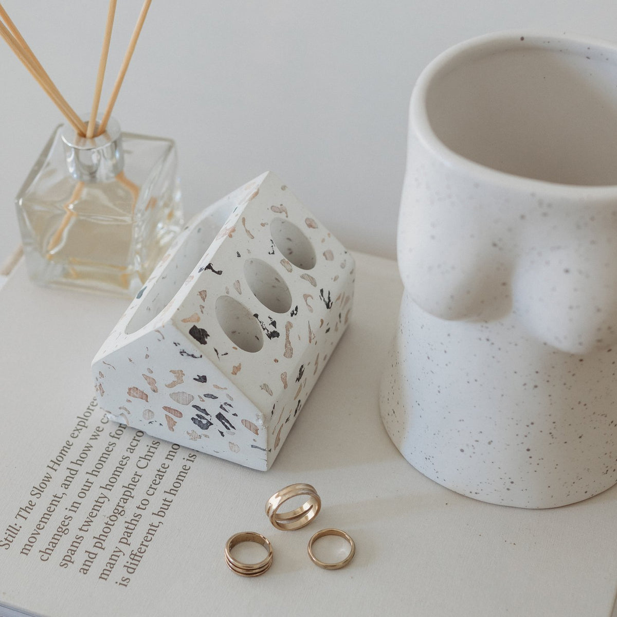 Terrazzo pen holder on an open book beside rings, a reed diffuser and a speckled vase