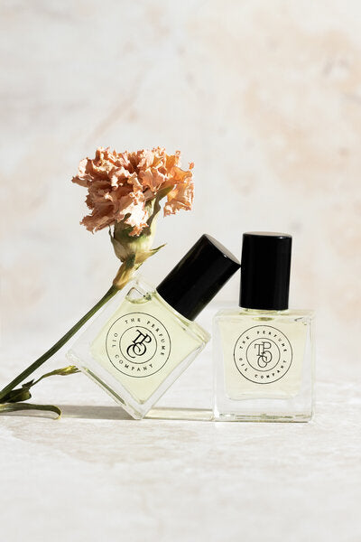 Perfume oil bottle with a single peach flower stem on white