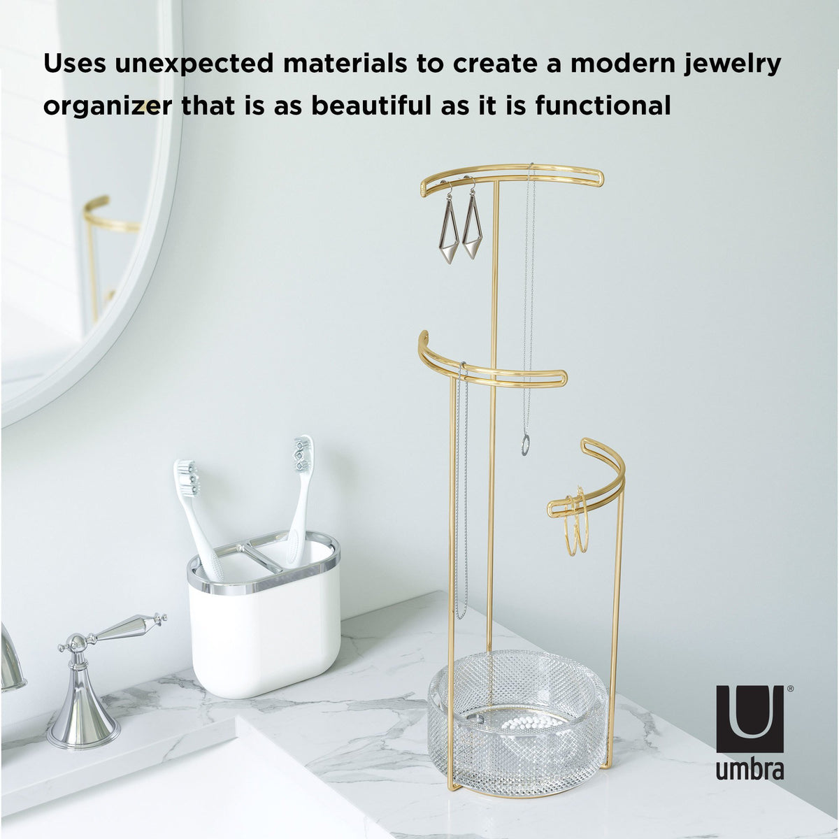 Tesora stand with earrings and chains on a bathroom bench beside a toothbrush holder